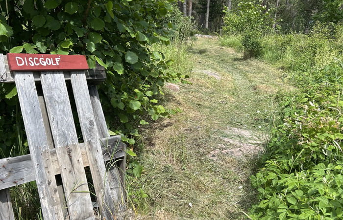 En träskylt intill en skog visar vägen till discgolfbanan
